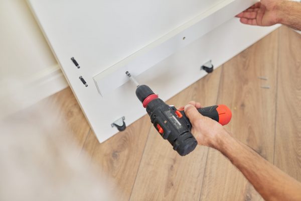 Close up detail of furniture and hands of carpenter worker with professional tool, screwdriver in hand, assembling furniture at home. Renovation, new furniture, work carpentry process