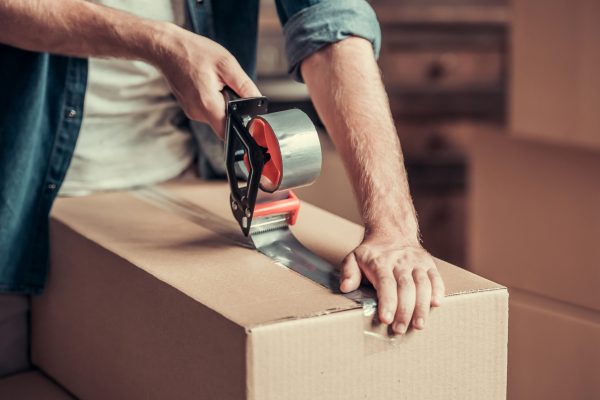 Cropped image of guy packing cardboard boxes while moving into new apartment
